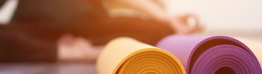 Tappetini da yoga arrotolati accanto a una persona in lezione — il tipo di iscrizione per turno con tetto che il modello Prenotazione Lezioni di Whocan gestisce